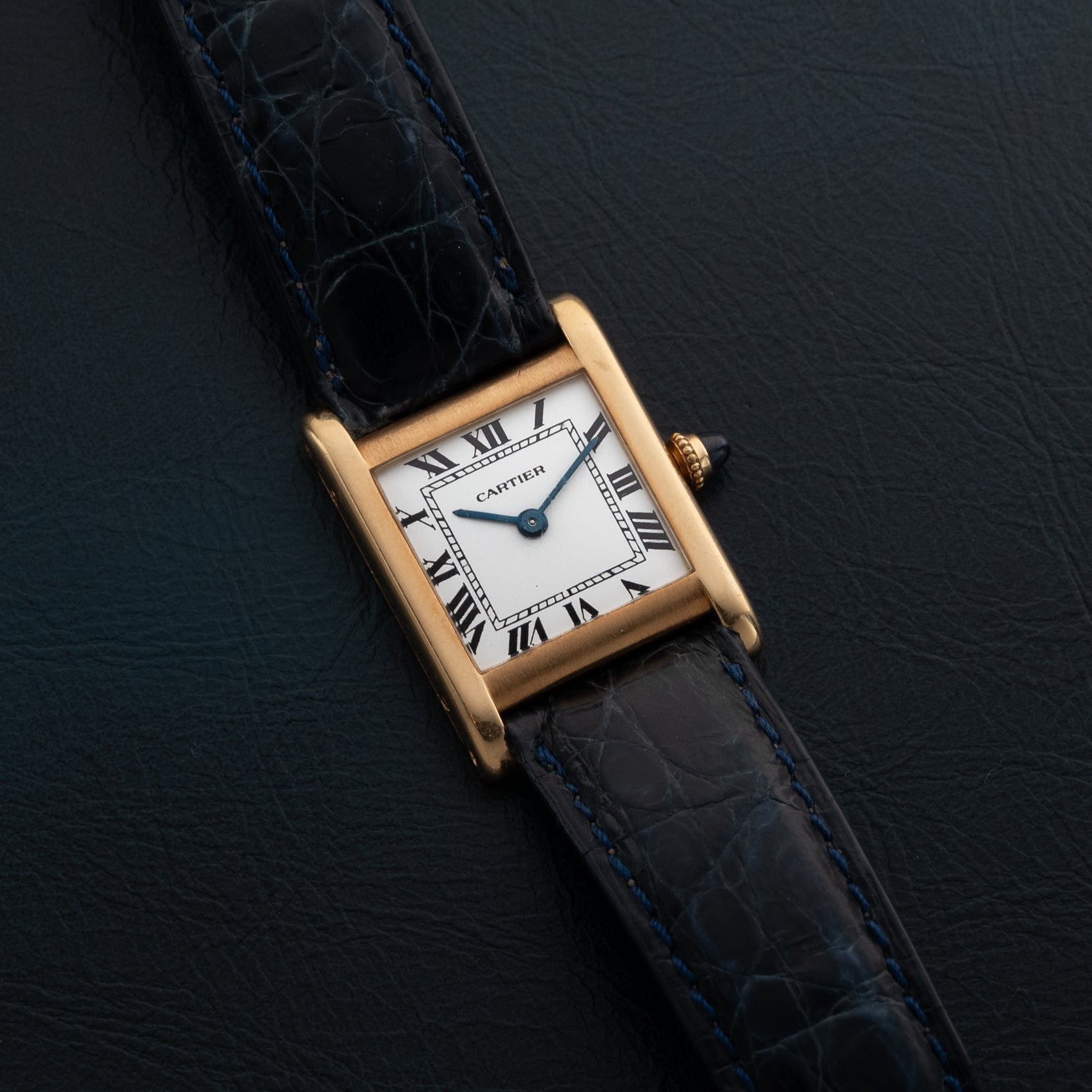 The Cartier Tank Normale with a black leather strap rests on a dark textured surface.