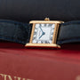 A Cartier Tank Normale watch with a black leather strap rests on a red book.