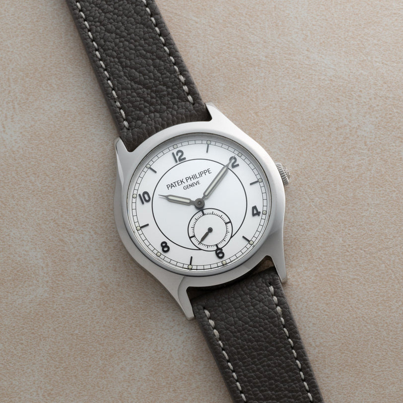 The Patek Philippe Calatrava Geneva Boutique Limited Edition wristwatch, featuring a white dial and black leather strap, displayed on a beige textured surface.