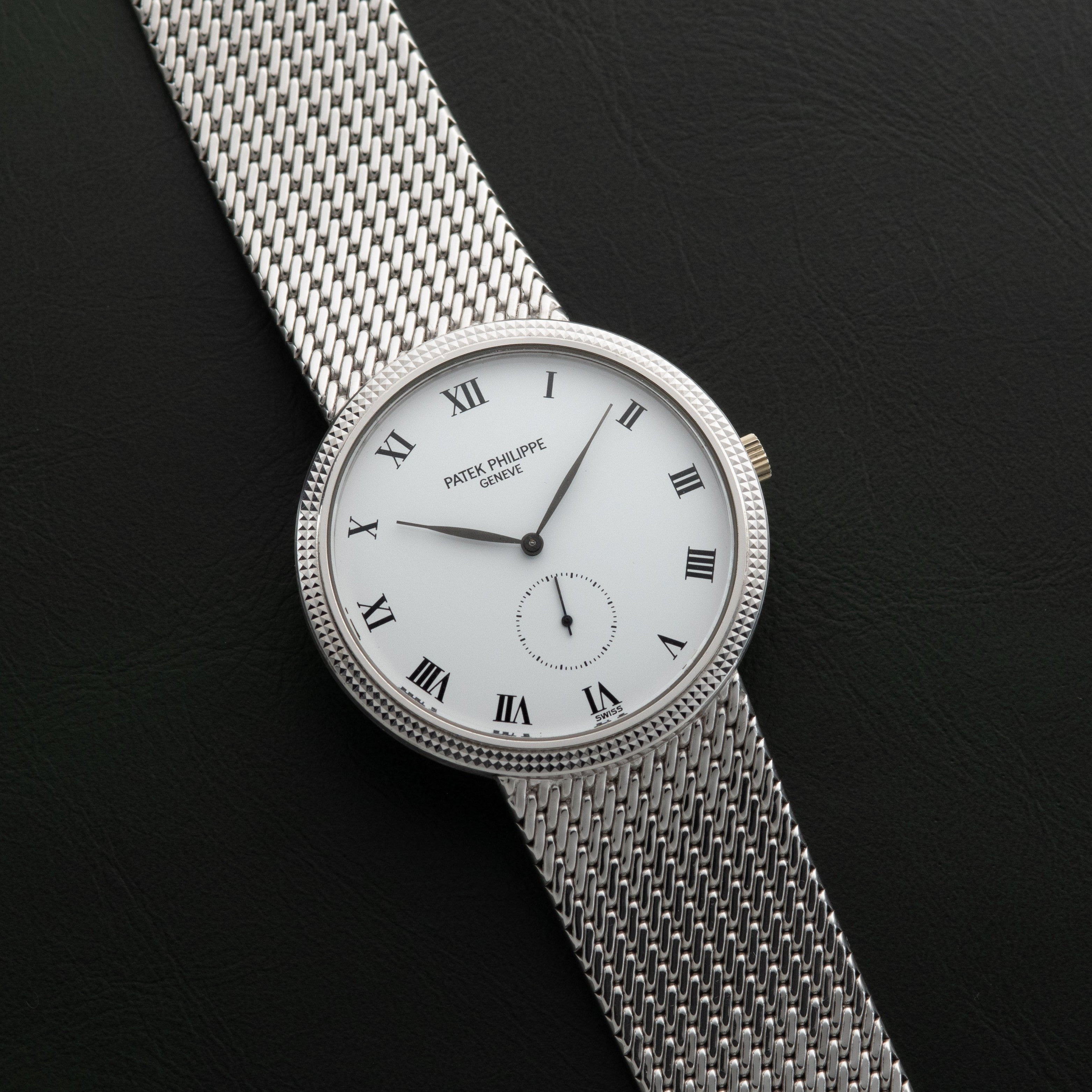 The Patek Philippe Calatrava is a silver mesh wristwatch featuring a white face with Roman numerals on a black background.