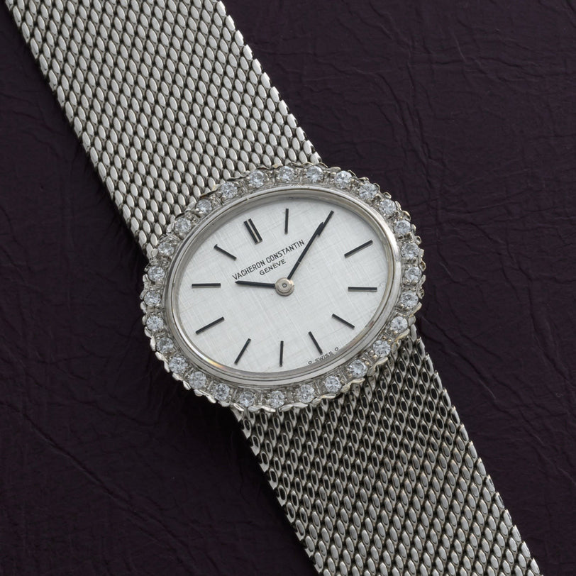 A Vacheron Constantin White Gold Diamond Bezel watch is shown on a mesh band, resting on a dark textured surface.