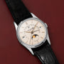 The Patek Philippe Retrograde Perpetual Calendar, featuring a black leather strap and moon phase display, is elegantly displayed on a red textured surface.