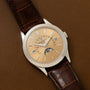 A Patek Philippe Retrograde Perpetual Calendar gold wristwatch with a brown leather strap and moon phase display rests on a brown leather surface.