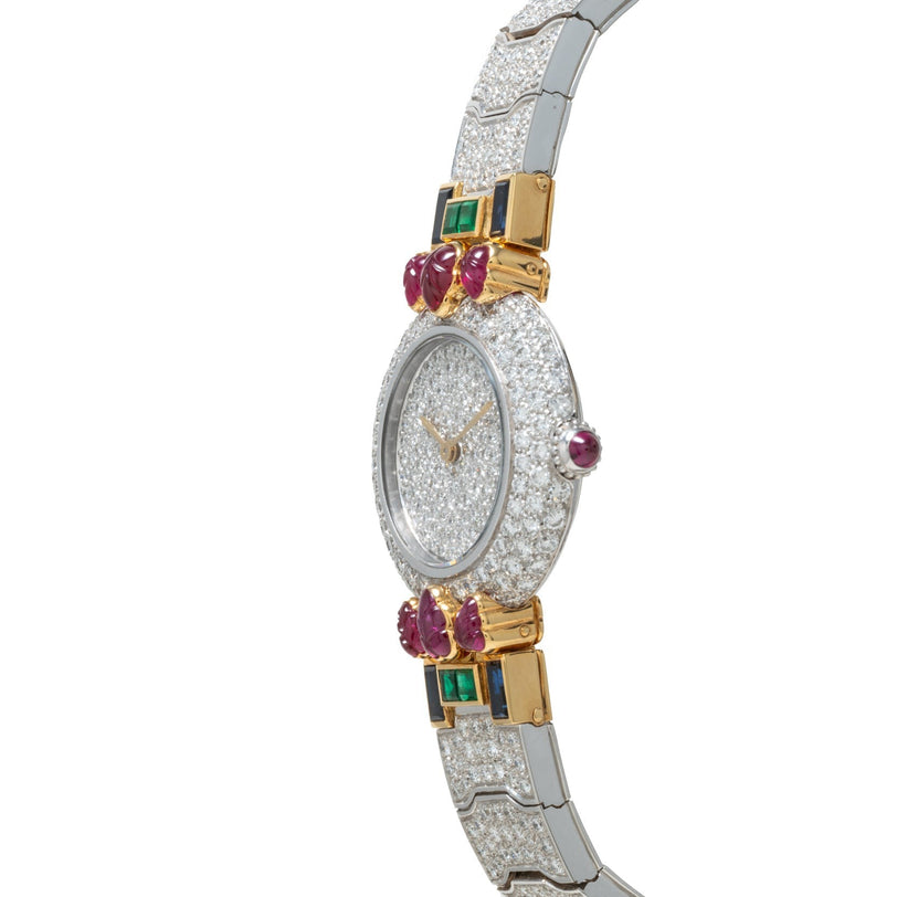 The Cartier Colisee Tutti Frutti Diamond is a luxury watch featuring a diamond-encrusted face, gold accents, green gems, and red oval stones on the band.