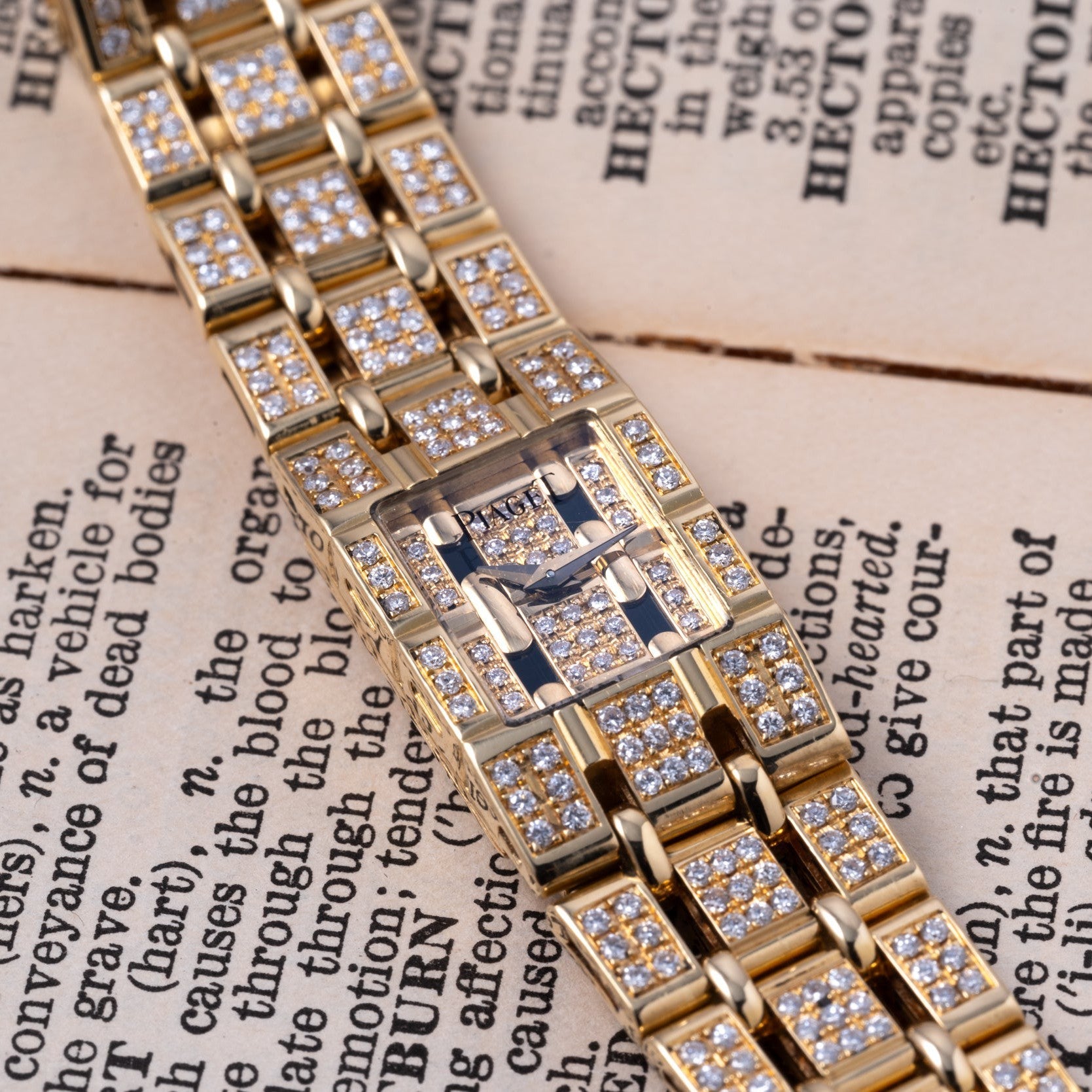The Piaget Polo Pave, a gold and diamond-encrusted watch, rests atop an open book with visible text.