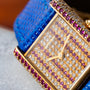 Close-up of the Cartier Tank Louis Diamonds watch featuring a blue strap, gold case, and a diamond and ruby-encrusted face.