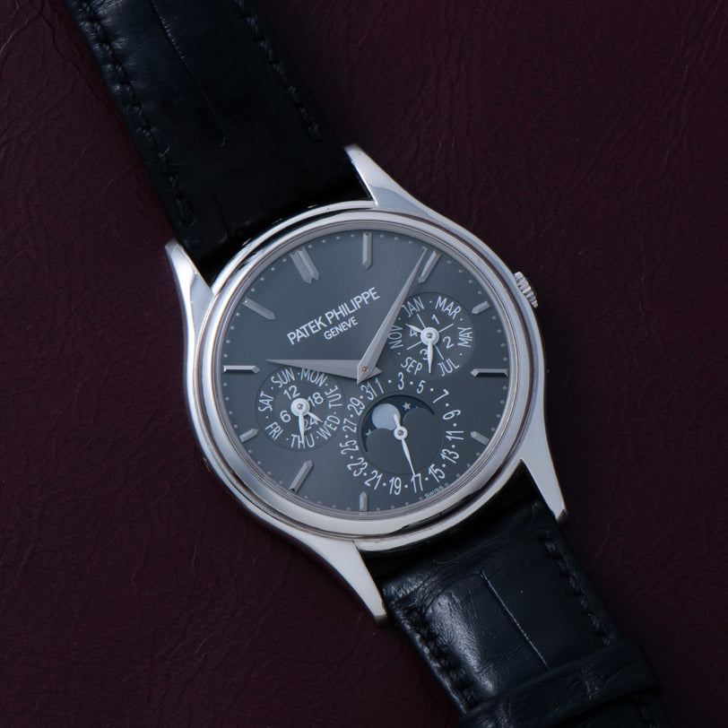 The Patek Philippe Perpetual Calendar wristwatch with a black leather strap is displayed on a dark maroon background.