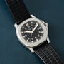 A Patek Philippe Aquanaut watch featuring a black dial and rubber strap displayed on a textured dark blue surface.