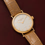 The Patek Philippe Calatrava wristwatch with a tan leather strap rests on a dark brown textured surface.