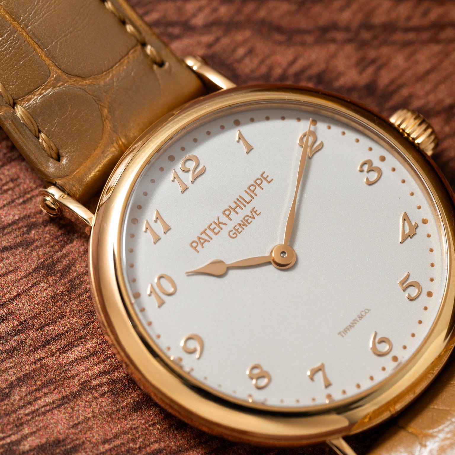 Patek Philippe Calatrava gold wristwatch with a brown leather strap displayed on a textured brown surface.