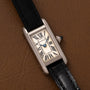 A Cartier Tank Ladies Allongee wristwatch with Roman numerals and a black leather strap displayed on a brown leather surface.