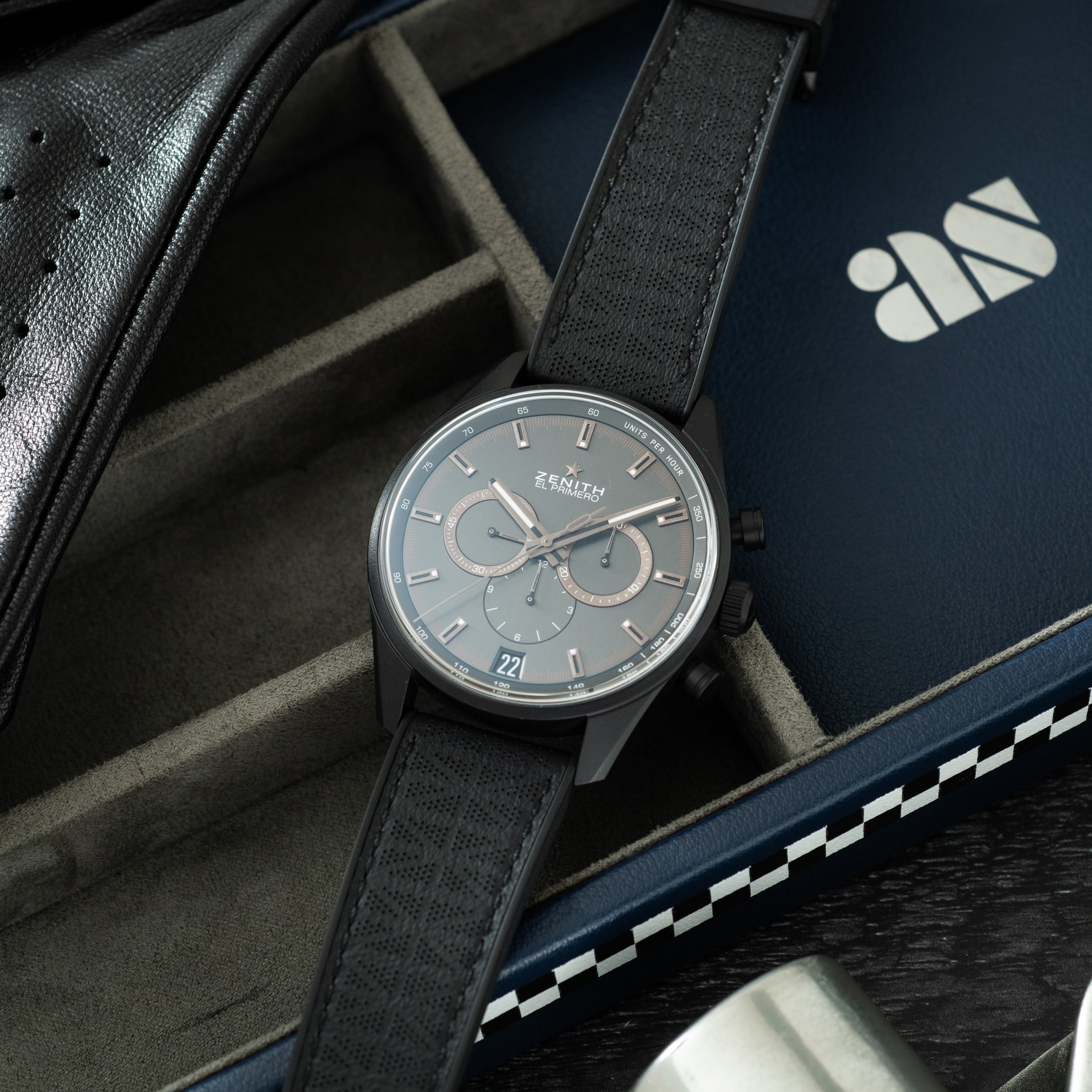 Zenith chronograph watch with gray dial and black fabric strap on leather case and branded packaging.