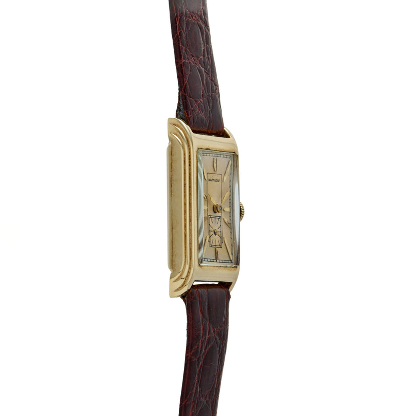Gold-tone rectangular watch with cream dial and Art Deco numerals on dark burgundy crocodile leather strap.