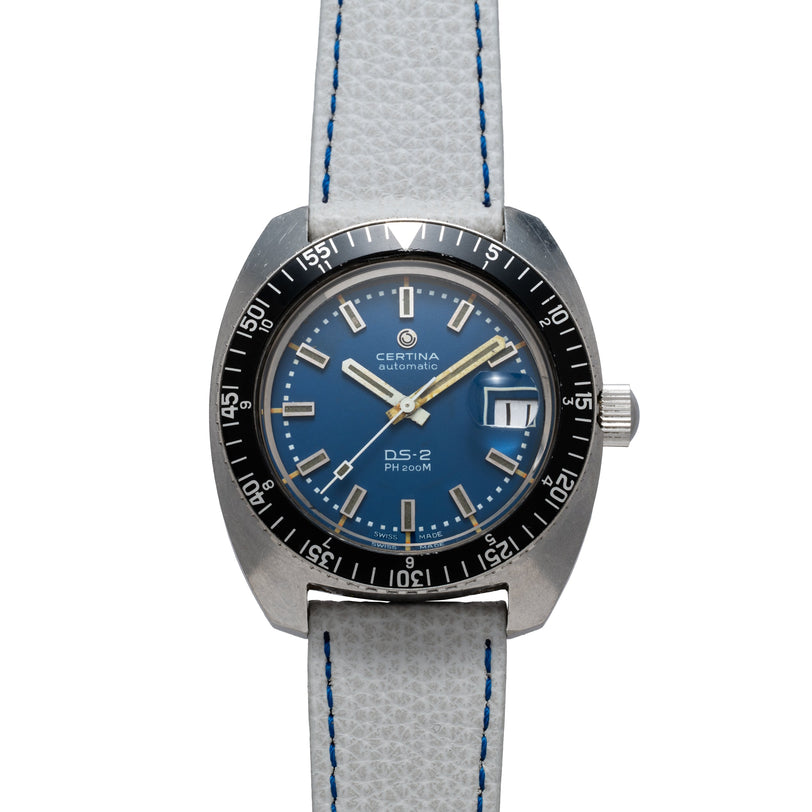 Certina DS-2 automatic watch with blue dial, black bezel, date window, and gray leather strap with blue stitching.