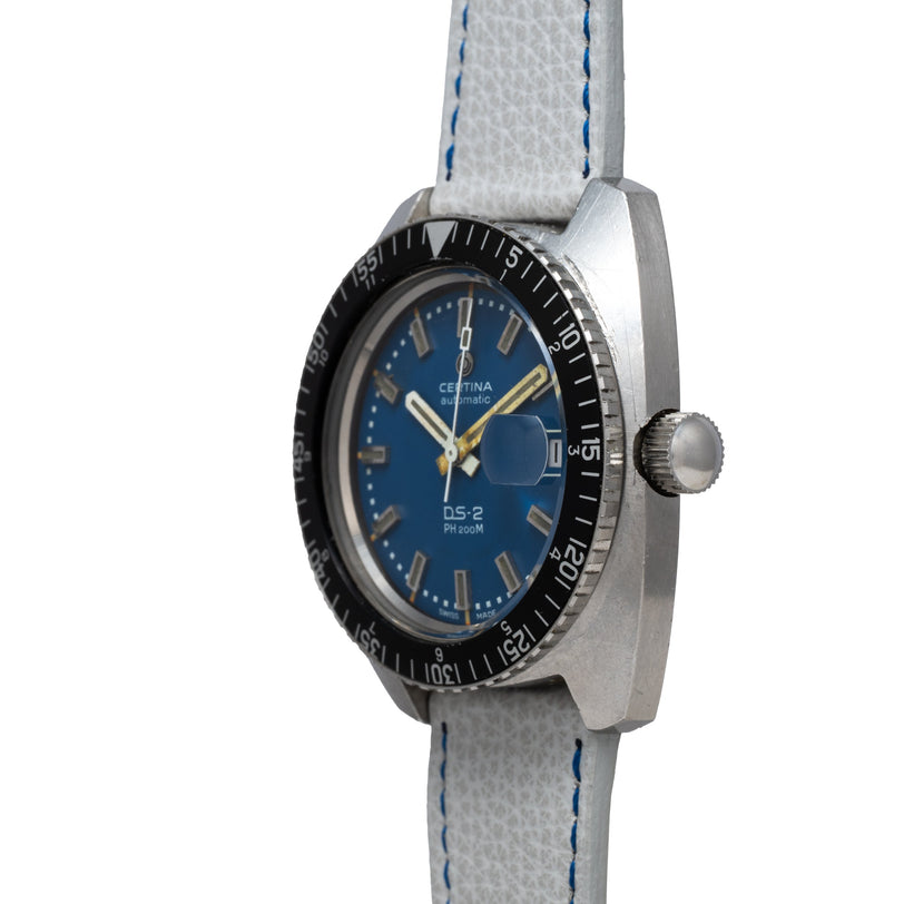 Certina DS-2 watch with blue dial, applied indices, yellow hands, black rotating bezel, and light gray fabric strap with blue