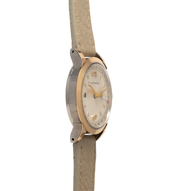 Movado two-tone watch with round cream dial, gold and silver case, and beige leather strap.