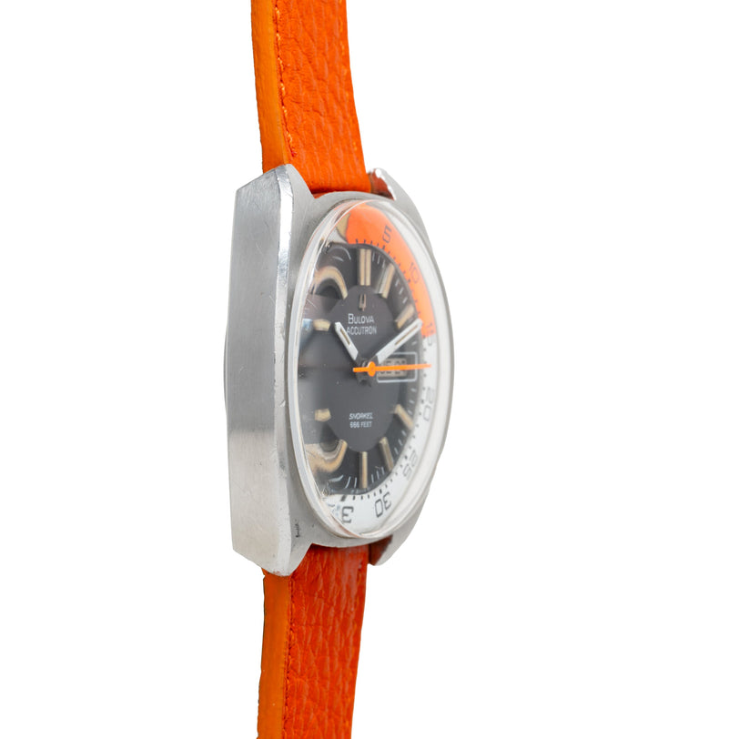 Bulova Accutron diver watch with brushed steel case, black dial, orange hands, and orange rubber strap.