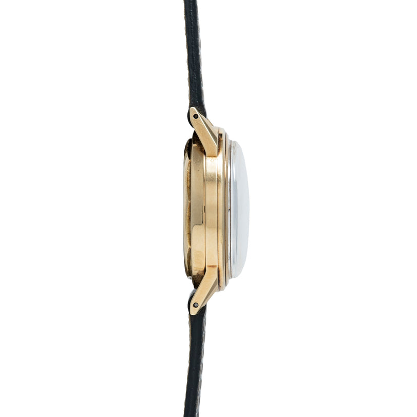 Gold-tone chronograph watch with round white dial and black leather strap, shown from side view.