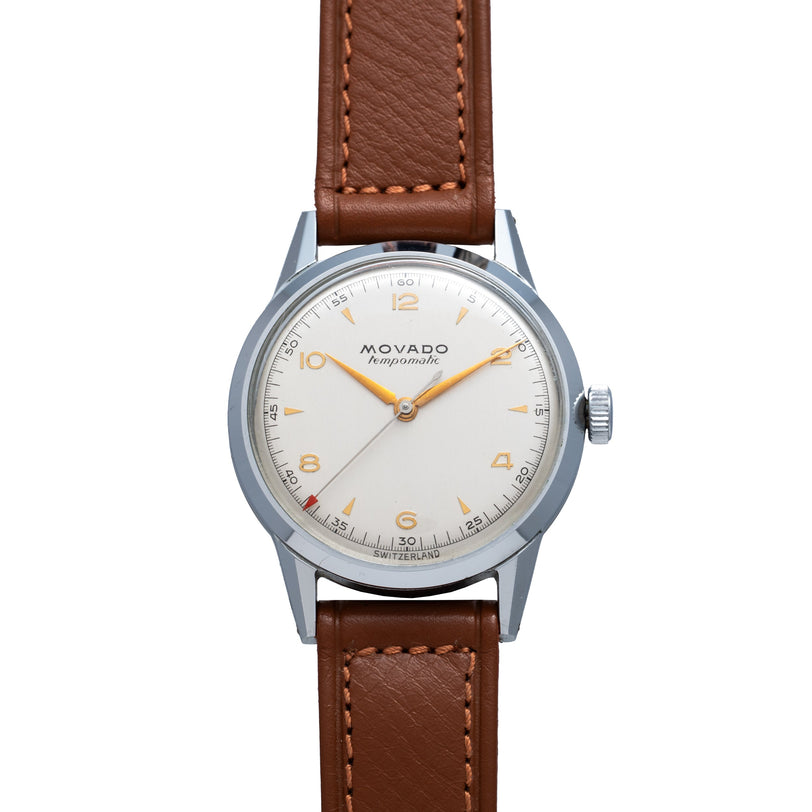 Stainless steel round watch with cream dial, orange numerals and hands, brown leather strap with contrast stitching.