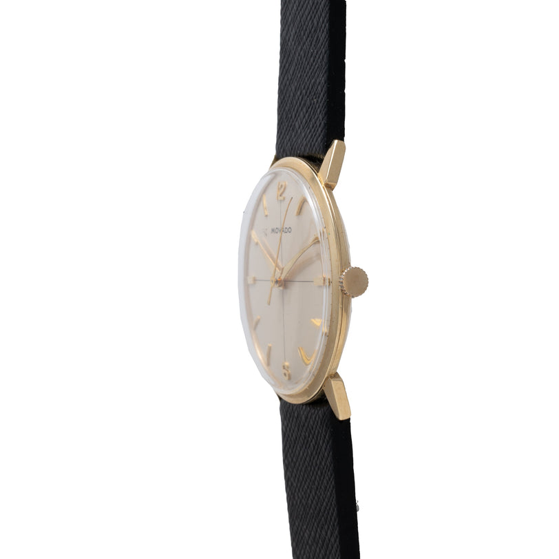Movado Calatrava watch with round gold case, cream dial, gold-tone hands, and black fabric strap.