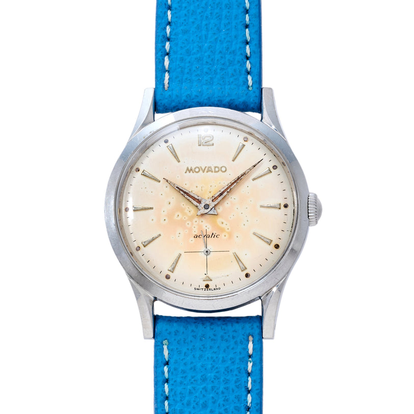 Movado Acvatic dress watch with cream dial, applied indices, and blue leather strap with white stitching.