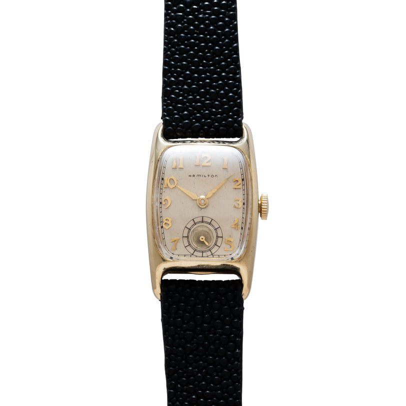 Hamilton Boulton vintage watch with rectangular gold-tone case, cream dial, Arabic numerals, and black fabric strap.