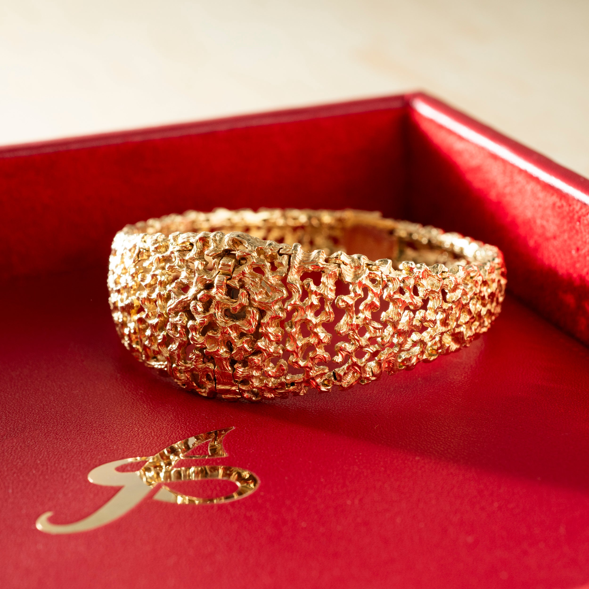 Gold-toned textured bracelet watch with crumpled surface design displayed in red presentation box.