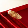 Gold-tone textured bracelet watch with small round dial, displayed in red velvet case.
