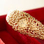 Gold textured bracelet watch with round cream dial and red gemstone accents on red fabric background.