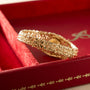 Gold-toned textured bracelet watch with integrated dial displayed on red fabric presentation box.