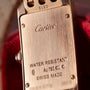 Close-up of the back of a Cartier Tank Americaine ladies watch in 18K rose gold, engraved with Cartier, WATER RESISTANT, Au 750, hallmarks, and SWISS MADE.