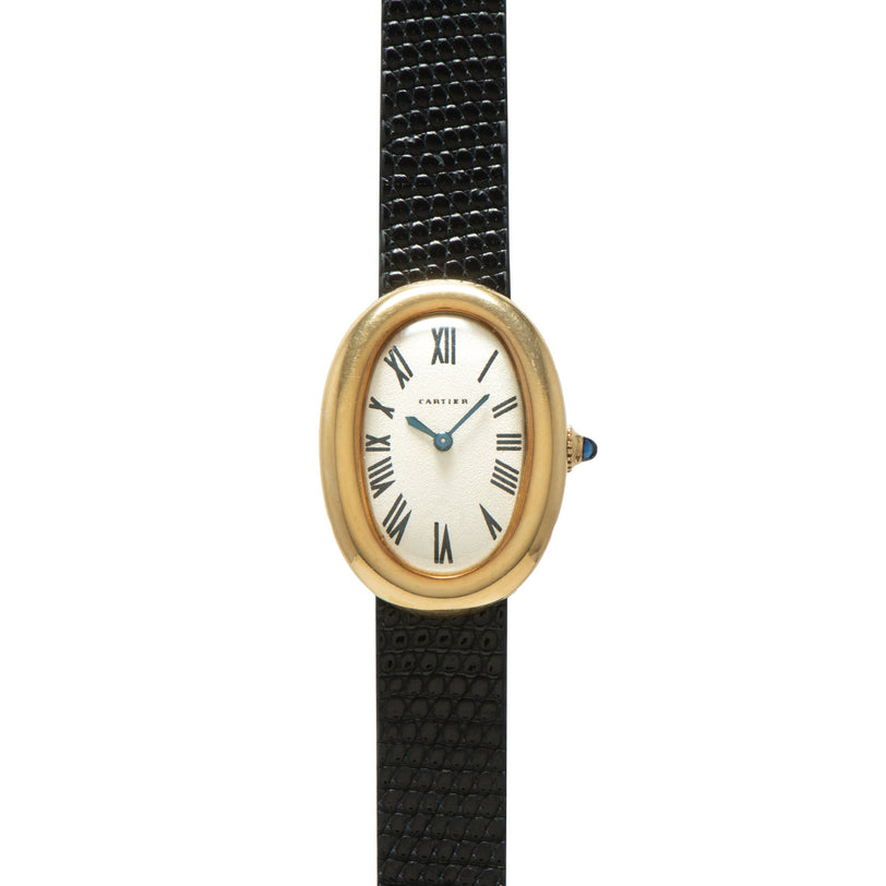 Gold-tone oval watch with cream dial, Roman numerals, blue hands, and black leather strap.