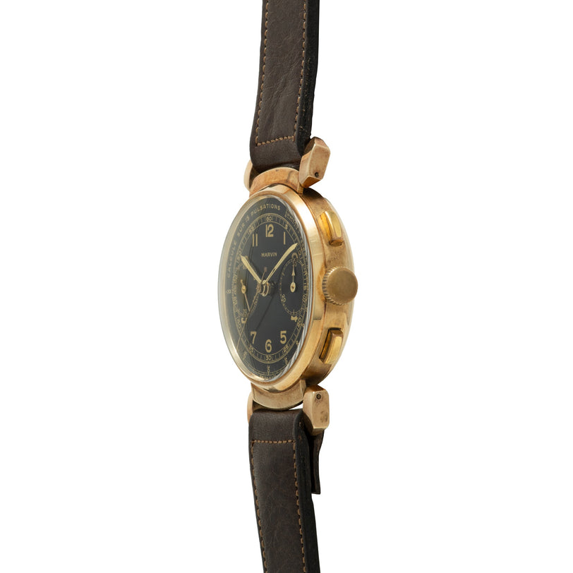 Gold-tone chronograph watch with black dial, Arabic numerals, and dark leather strap with hinged lugs.