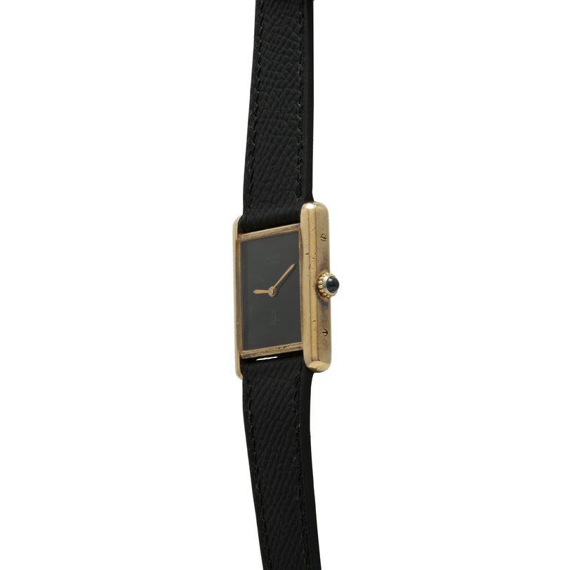 Gold-tone rectangular watch with black dial, gold hands, and black fabric strap.