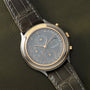 Stainless steel and gold-tone chronograph watch with gray dial, three subdials, and dark leather crocodile-embossed strap.