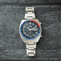 Seiko chronograph watch with stainless steel case and bracelet, black dial, blue and red bezel, and date window.