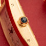Gold watch bracelet with dark blue faceted stone crown and screw details on brushed gold band.