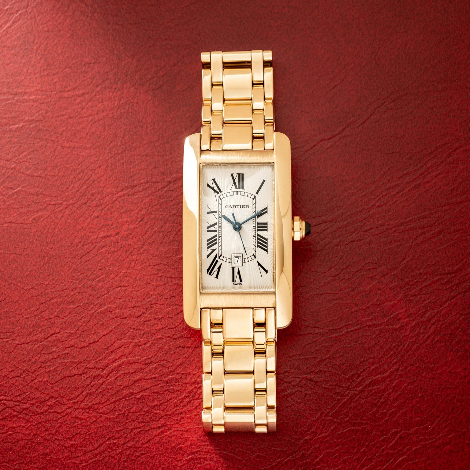 Gold-tone rectangular watch with white dial, Roman numerals, and matching link bracelet on red background.