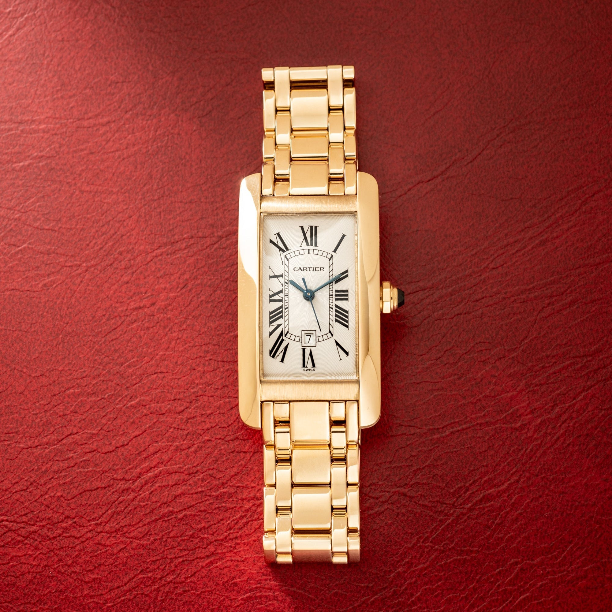 Gold-tone rectangular watch with white dial, Roman numerals, and matching link bracelet on red background.