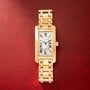 Gold-tone rectangular watch with white dial, Roman numerals, and matching link bracelet on red background.