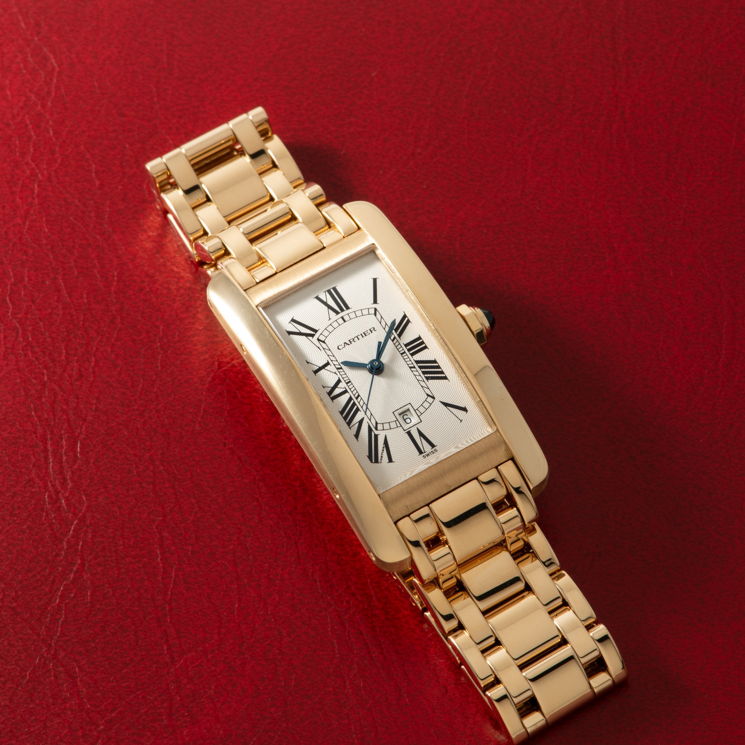 Gold-tone rectangular watch with white dial, Roman numerals, and matching link bracelet on red background.