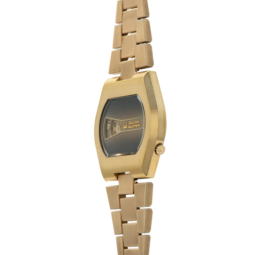 Gold-tone Bulova Accutron watch with rectangular case, dark dial, and segmented link bracelet.