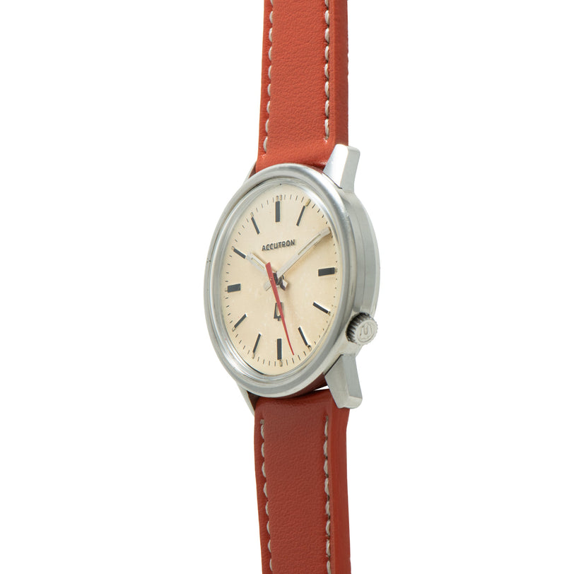 Bulova Accutron dress watch with cream dial, black indices, red leather strap, and stainless steel case.