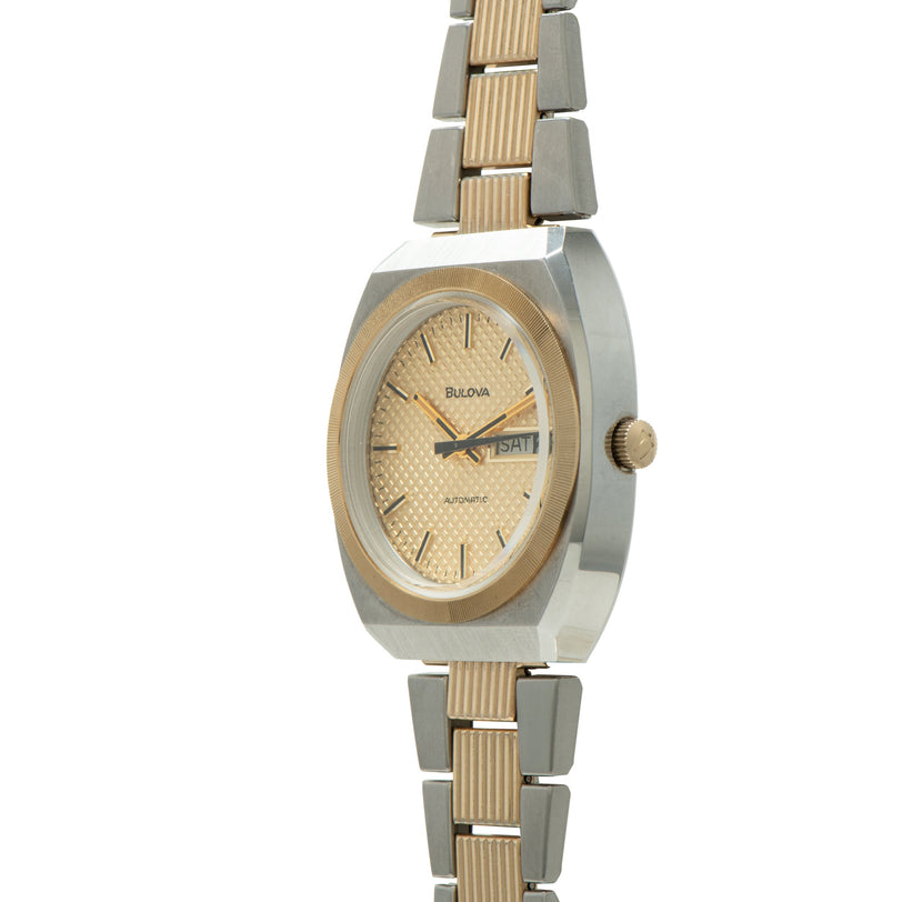 Bulova two-tone watch with oval case, champagne dial, day-date window, and alternating silver and gold-tone bracelet.
