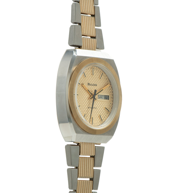 Bulova two-tone watch with rectangular case, champagne dial, day-date window, and alternating silver and gold-tone bracelet.