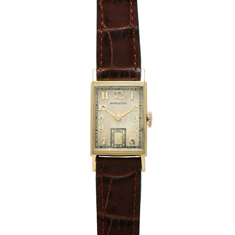 Hamilton rectangular watch with cream dial, Arabic numerals, and brown leather strap with decorative stitching.