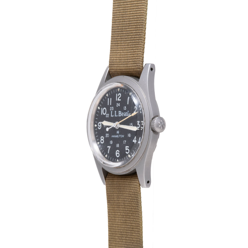 Hamilton Khaki Field mechanical watch with black dial, silver hands, tan fabric strap, and crown on right side.