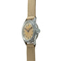 Vintage Elgin wristwatch with cream dial, Arabic numerals, weathered metal case, and tan fabric strap.