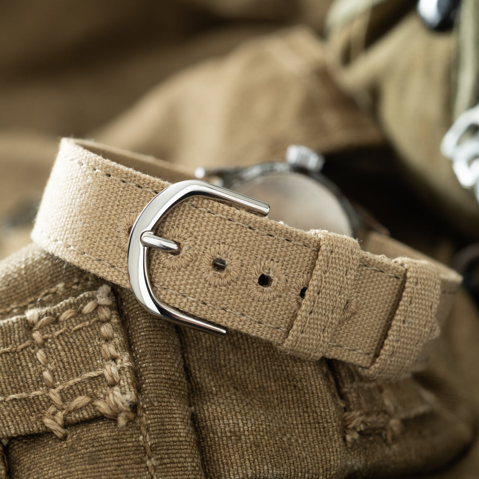 Elgin USMC watch with tan canvas strap and silver buckle displayed on khaki fabric.