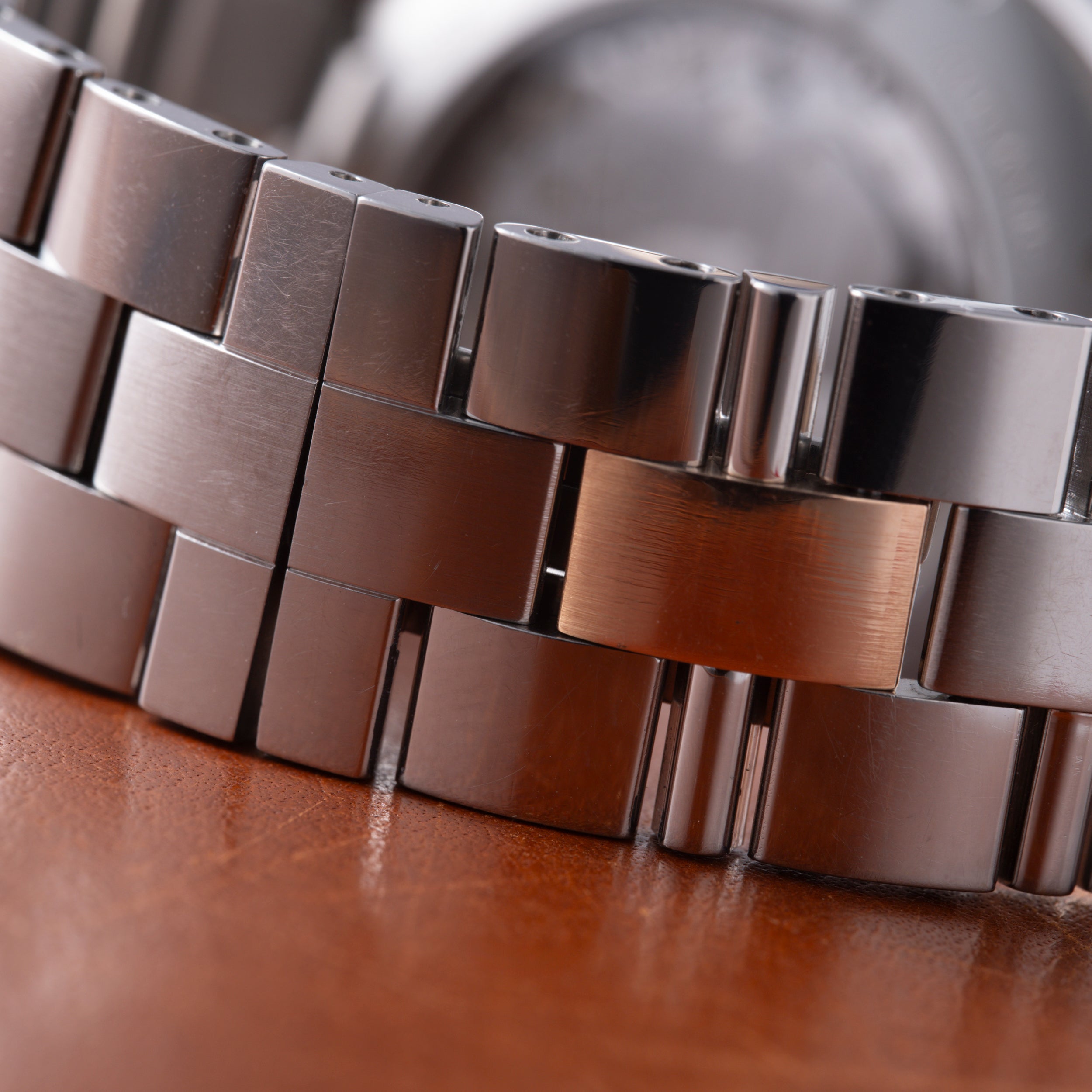 Close-up of stainless steel watch bracelet with polished and brushed link segments on brown leather surface.